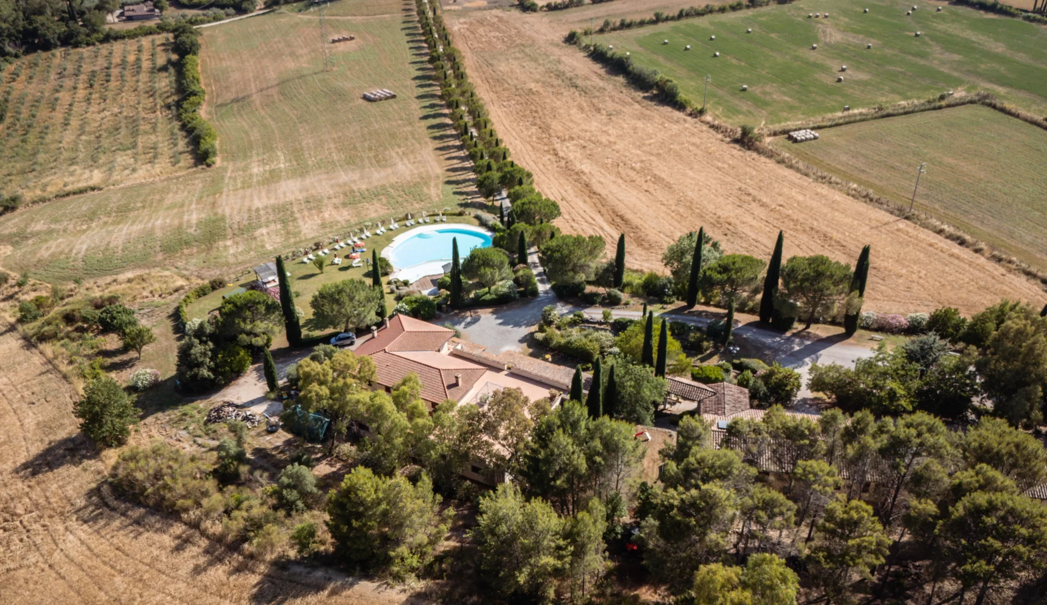 Vista aerea di una proprietà rurale con piscina circondata da campi e alberi.