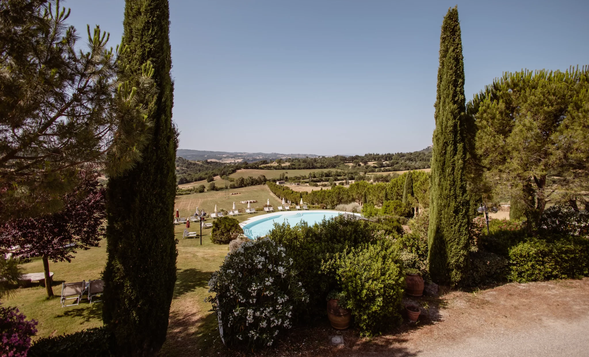 Paesaggio collinare con piscina circondata da cipressi e vegetazione.