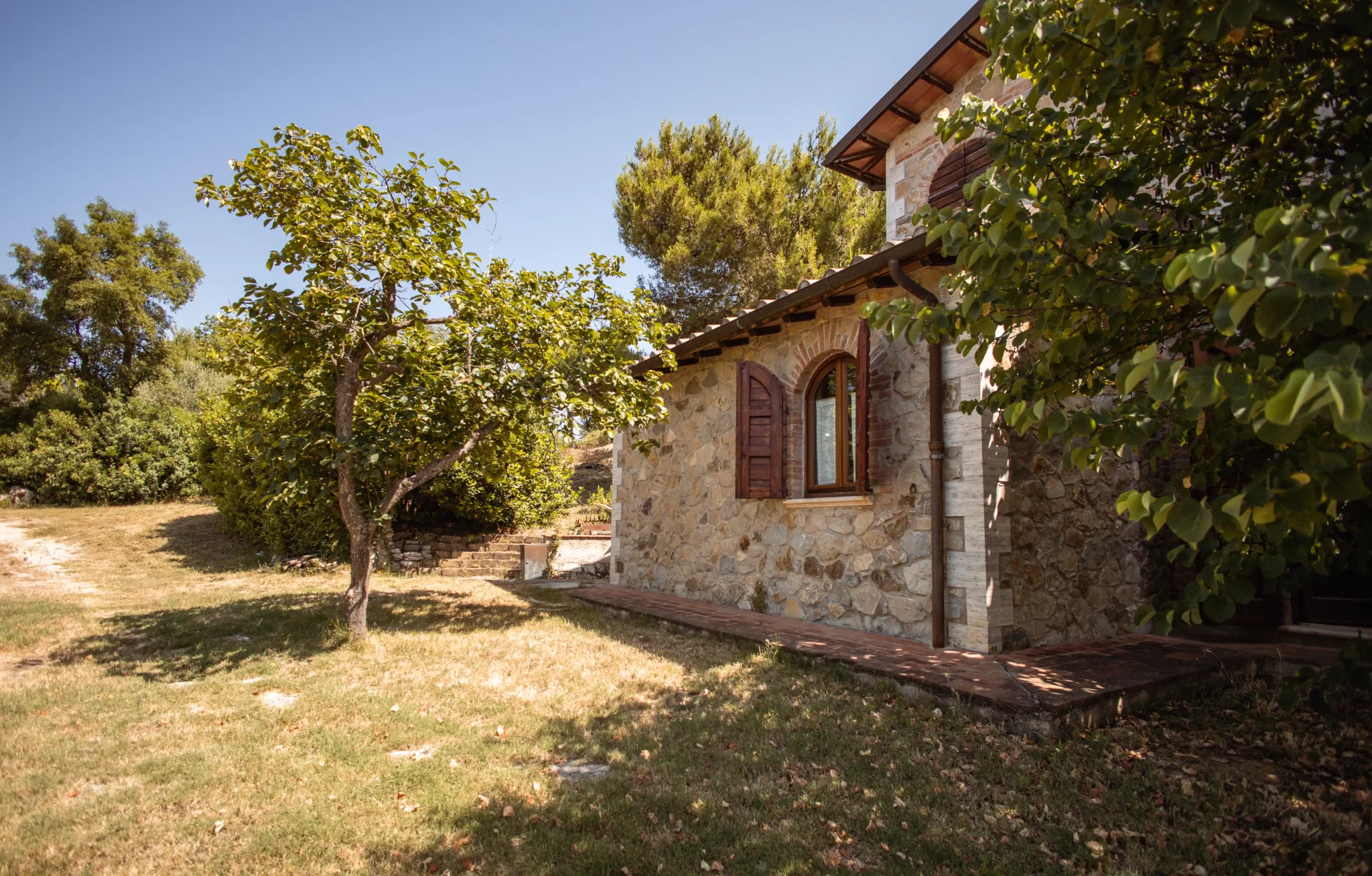 Casale in pietra immerso nel verde con alberi e cielo azzurro.