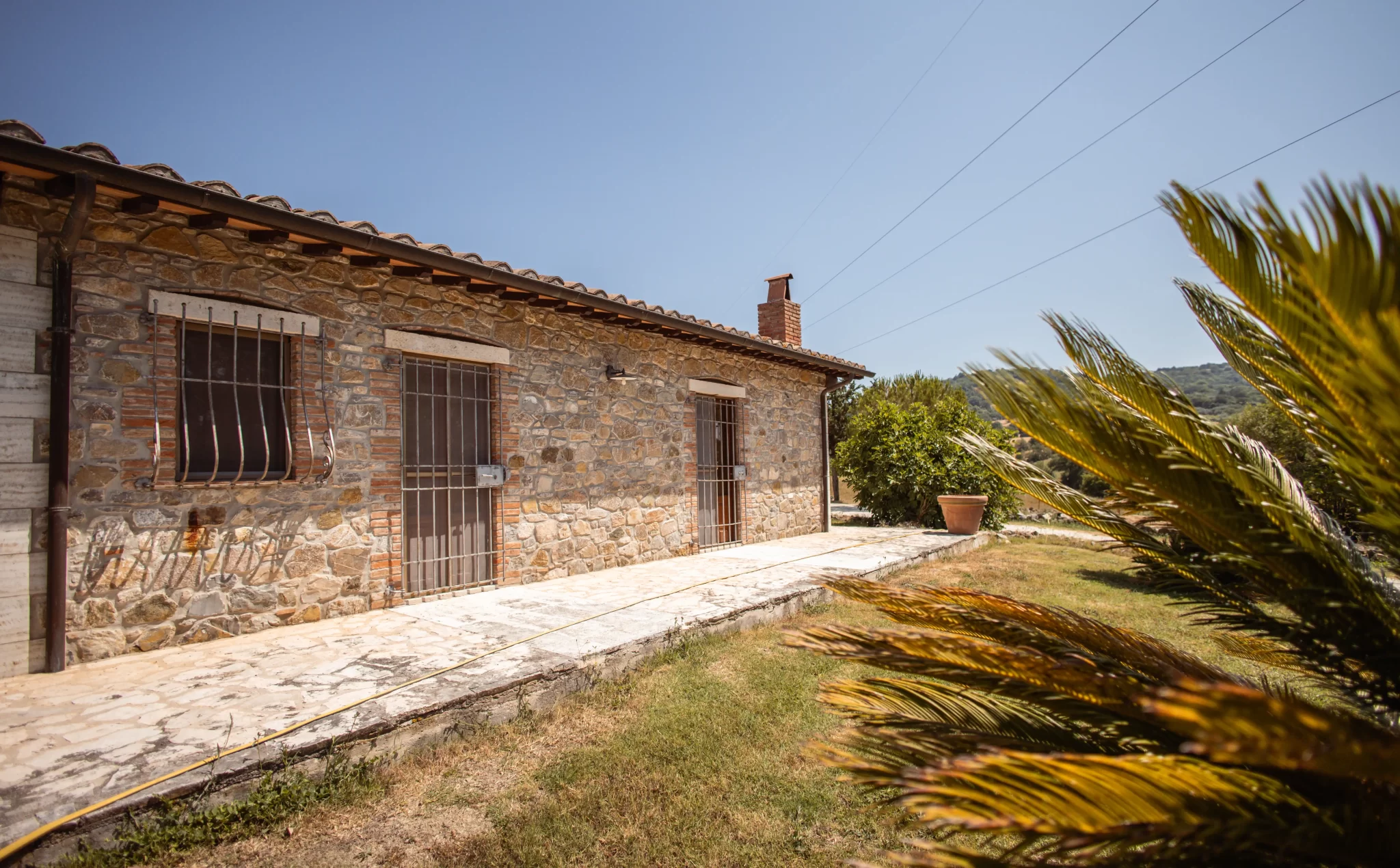 Casa rurale in pietra con tetto in tegole e giardino, in un paesaggio soleggiato.