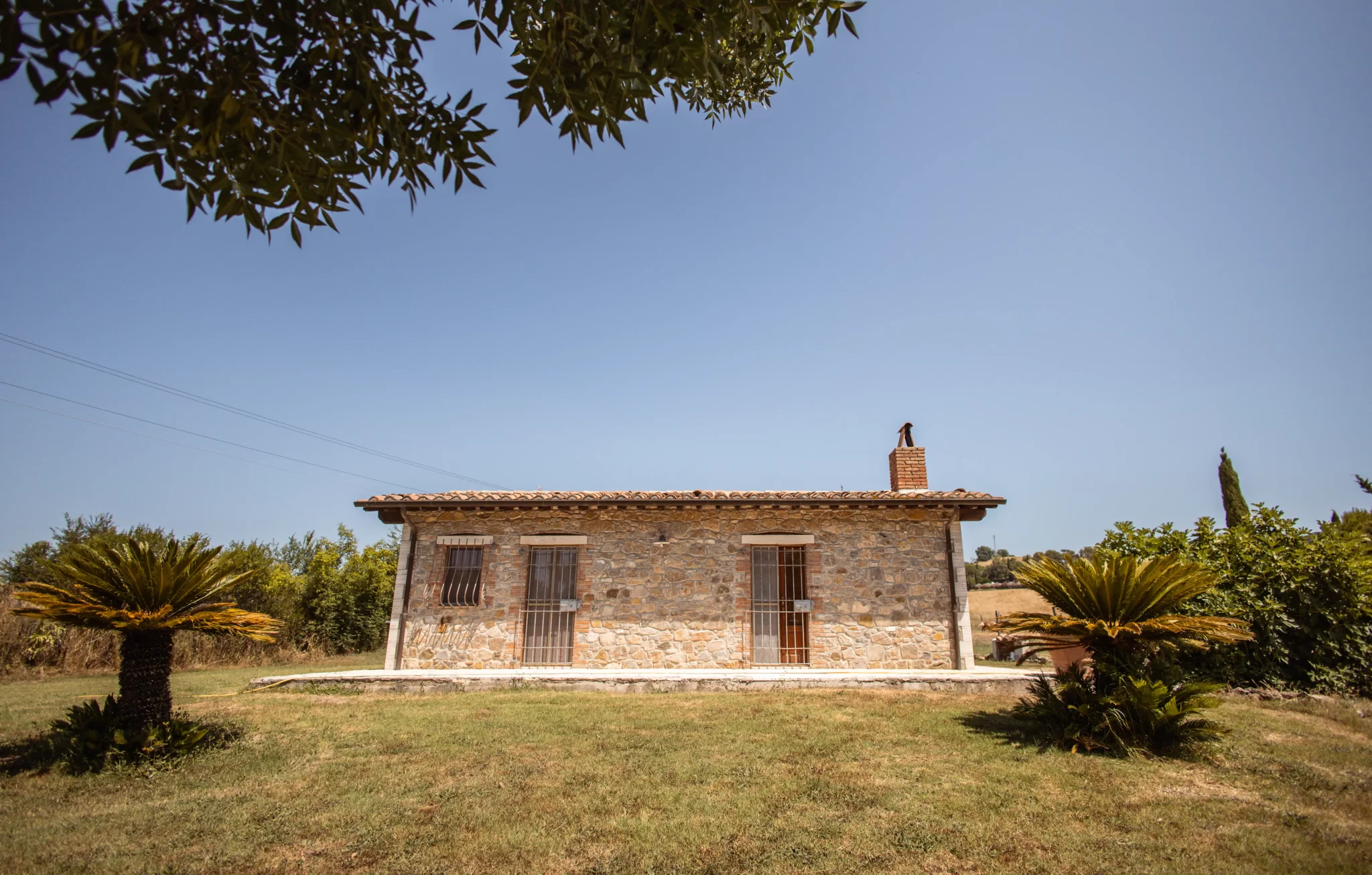 Casa di pietra con giardino, circondata da vegetazione, in una giornata serena.
