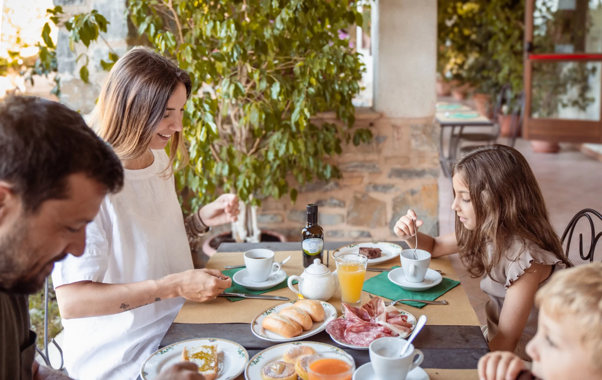 Famiglia che fa colazione all'aperto con vari alimenti su un tavolo.