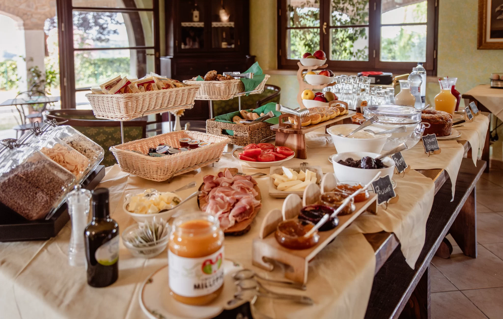 Buffet di colazione ricco di varietà con salumi, formaggi, frutta, cereali e succhi in un ambiente accogliente.