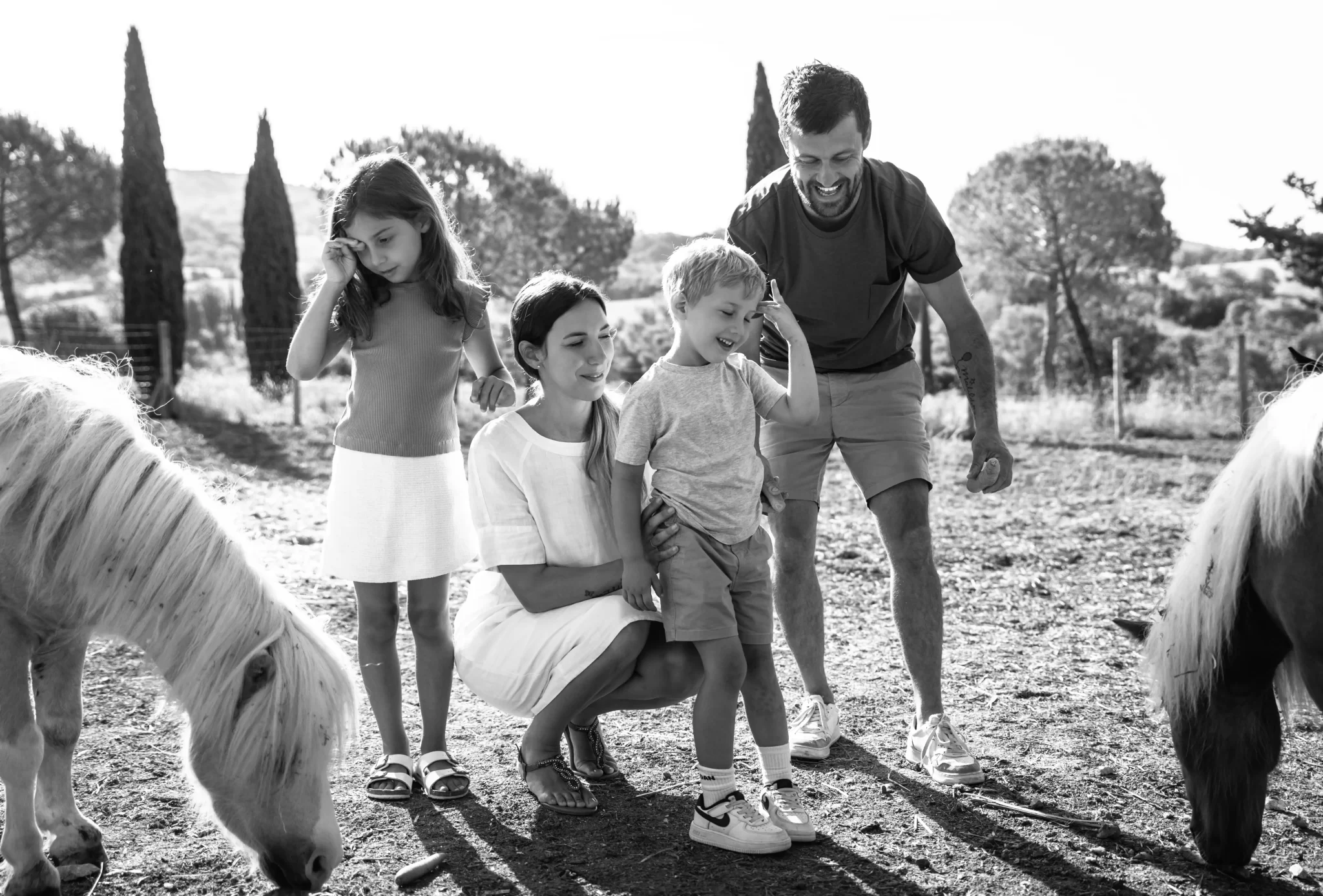 Famiglia che interagisce con pony in un ambiente rurale.