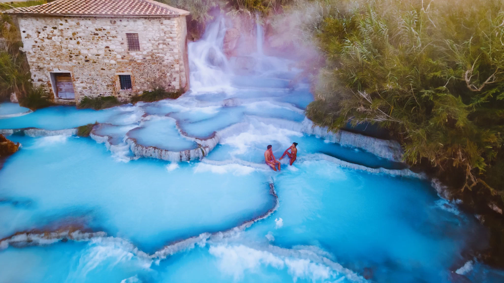 Cascate termali di Saturnia con vasche naturali e una vecchia casa di pietra.