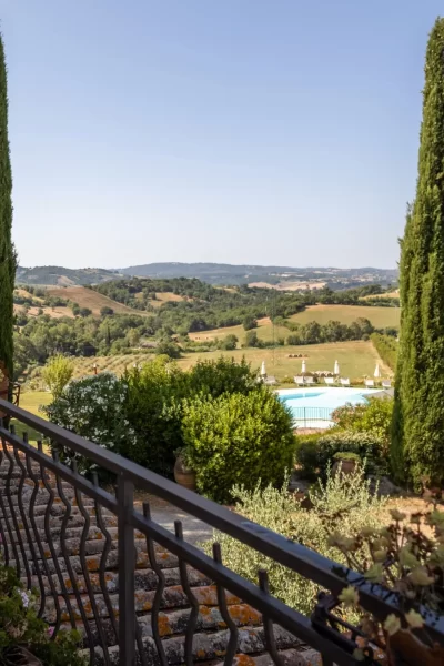 Vista panoramica di una terrazza con piante, alberi, piscina e colline in lontananza.