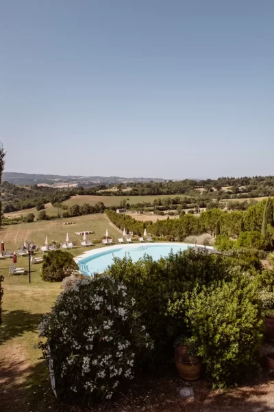 Paesaggio collinare con piscina circondata da cipressi e vegetazione.