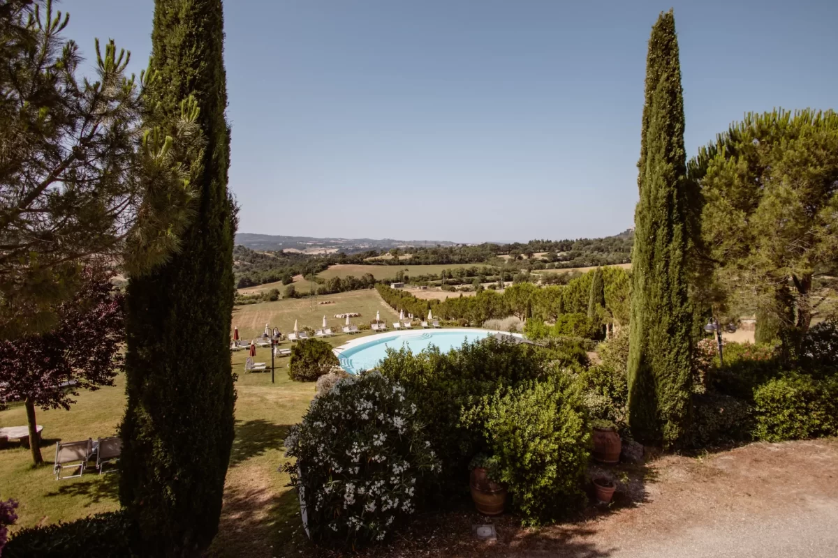 Paesaggio collinare con piscina circondata da cipressi e vegetazione.