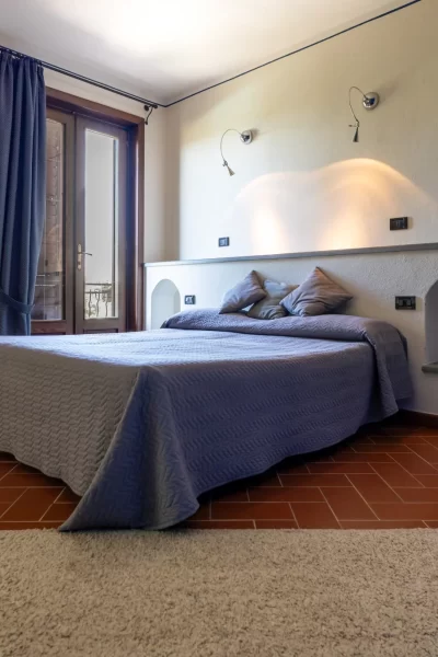 Una camera da letto accogliente con letto matrimoniale, pavimento in cotto e porta-finestra con tende blu.