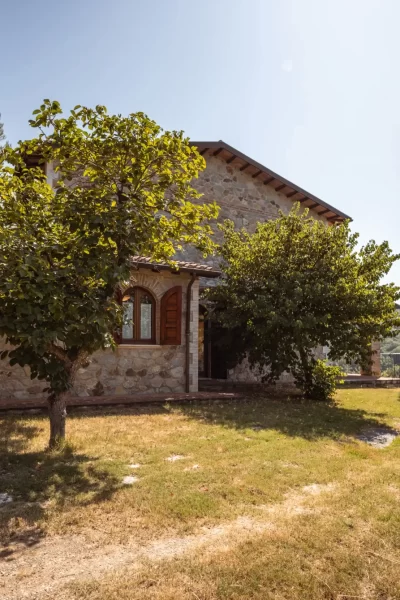 Casa in pietra immersa in un giardino con alberi e cipresso.