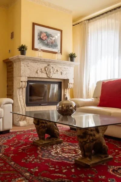 Soggiorno accogliente con camino, divano bianco e tappeto rosso decorativo.