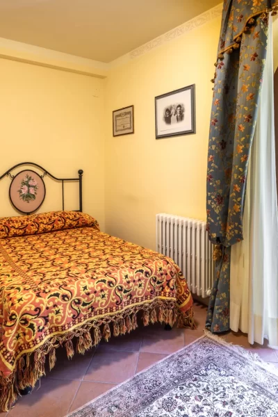 Camera da letto accogliente con letto matrimoniale decorato, finestra ad arco e tende fiorite.