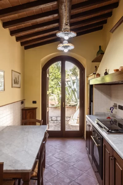 Cucina rustica con travi a vista, tavolo in marmo e porta finestra che si apre su un giardino.