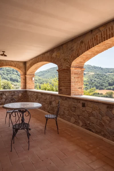 Loggia con vista su colline verdi e tavolo in ferro battuto.
