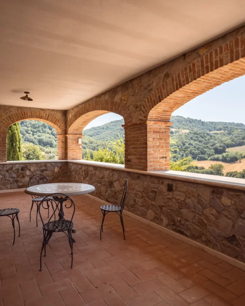 Loggia con vista su colline verdi e tavolo in ferro battuto.