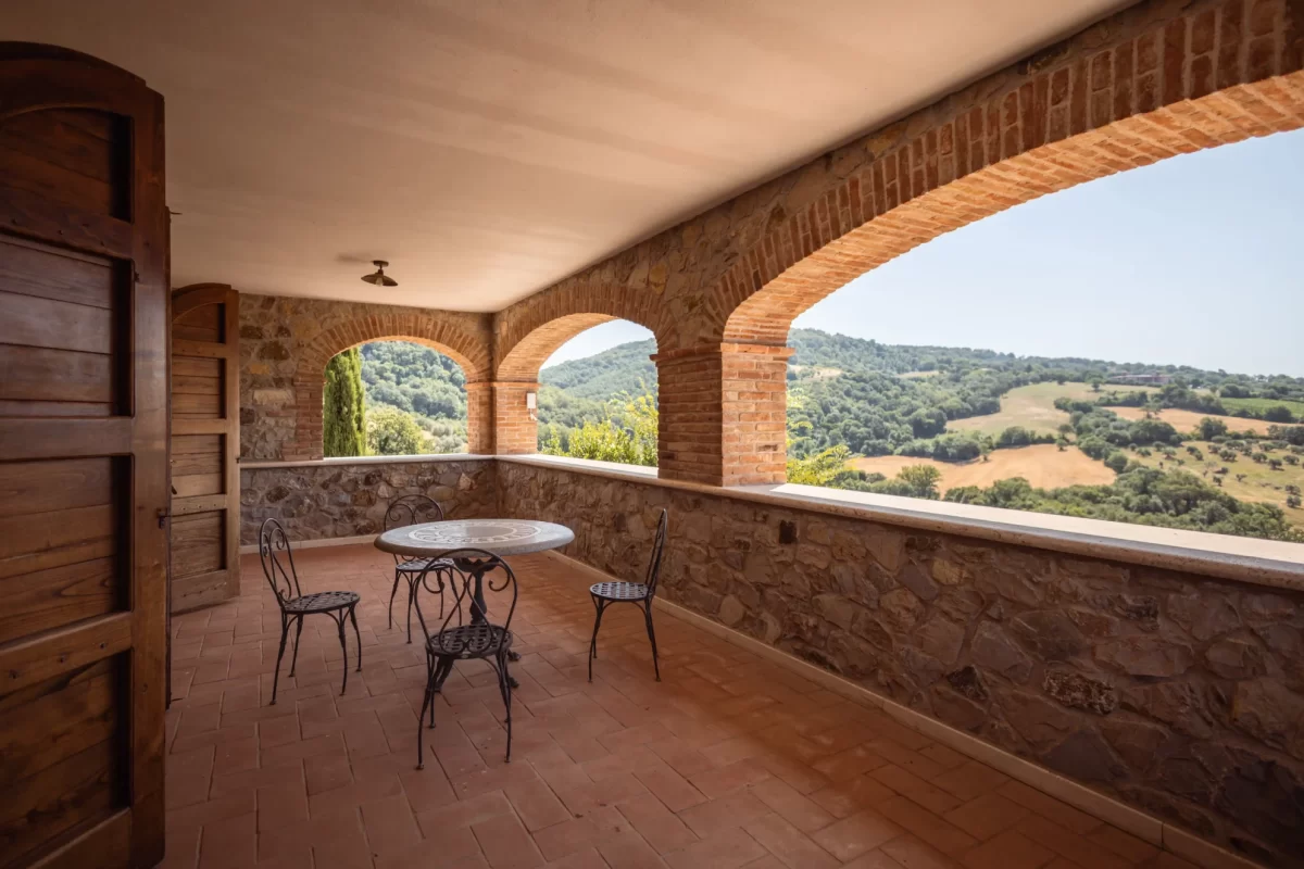 Loggia con vista su colline verdi e tavolo in ferro battuto.