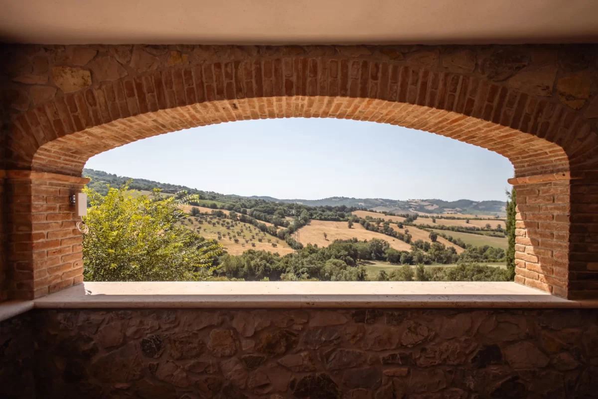 Veduta di colline toscane attraverso un arco in mattoni.