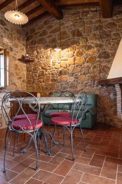 Sala da pranzo rustica con pareti in pietra, camino e tavolo con sedie in ferro battuto.