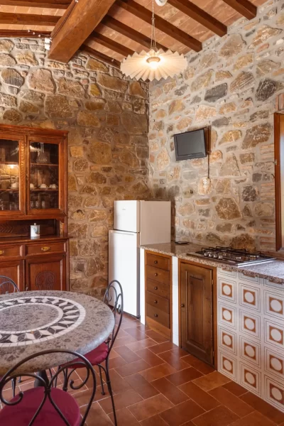 Cucina rustica con parete in pietra, soffitto con travi in legno e tavolo in marmo.