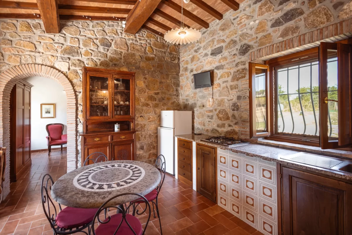 Cucina rustica con parete in pietra, soffitto con travi in legno e tavolo in marmo.