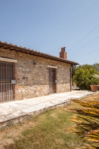 Casa rurale in pietra con tetto in tegole e giardino, in un paesaggio soleggiato.