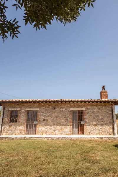 Casa di pietra con giardino, circondata da vegetazione, in una giornata serena.