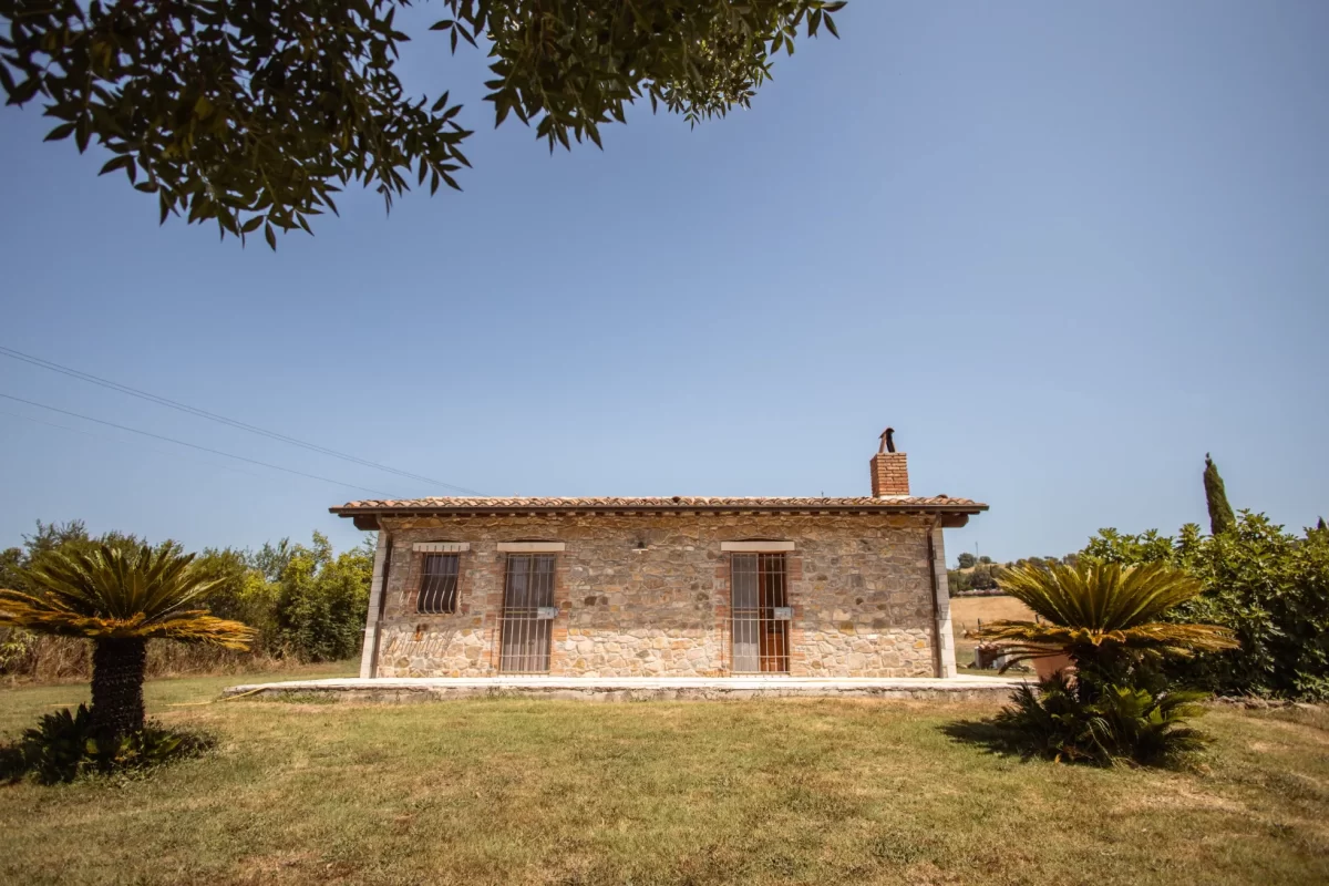 Casa di pietra con giardino, circondata da vegetazione, in una giornata serena.