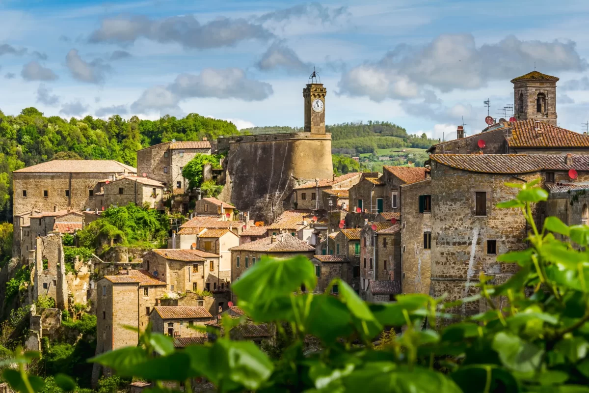 Vista panoramica di un borgo medievale con un orologio su una torre, circondato da colline verdi.