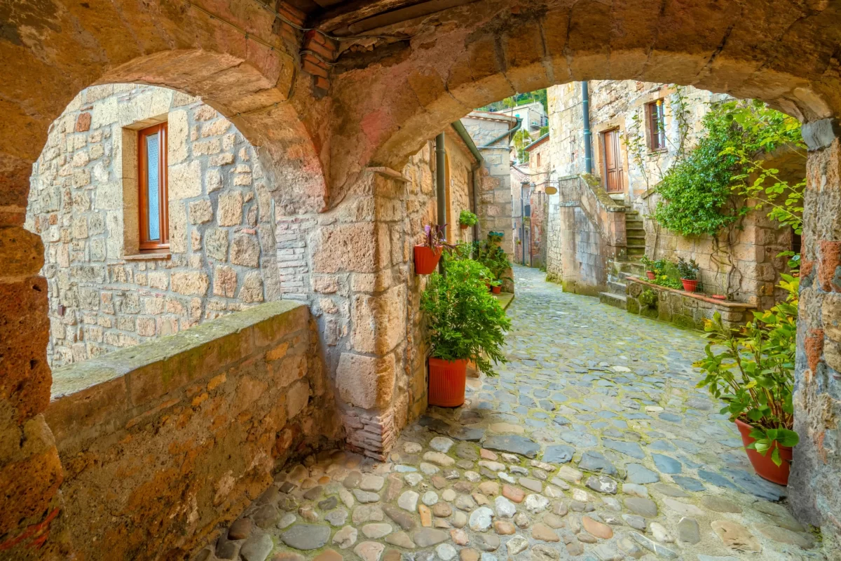 Vicolo di un borgo italiano con archi in pietra e piante in vaso.