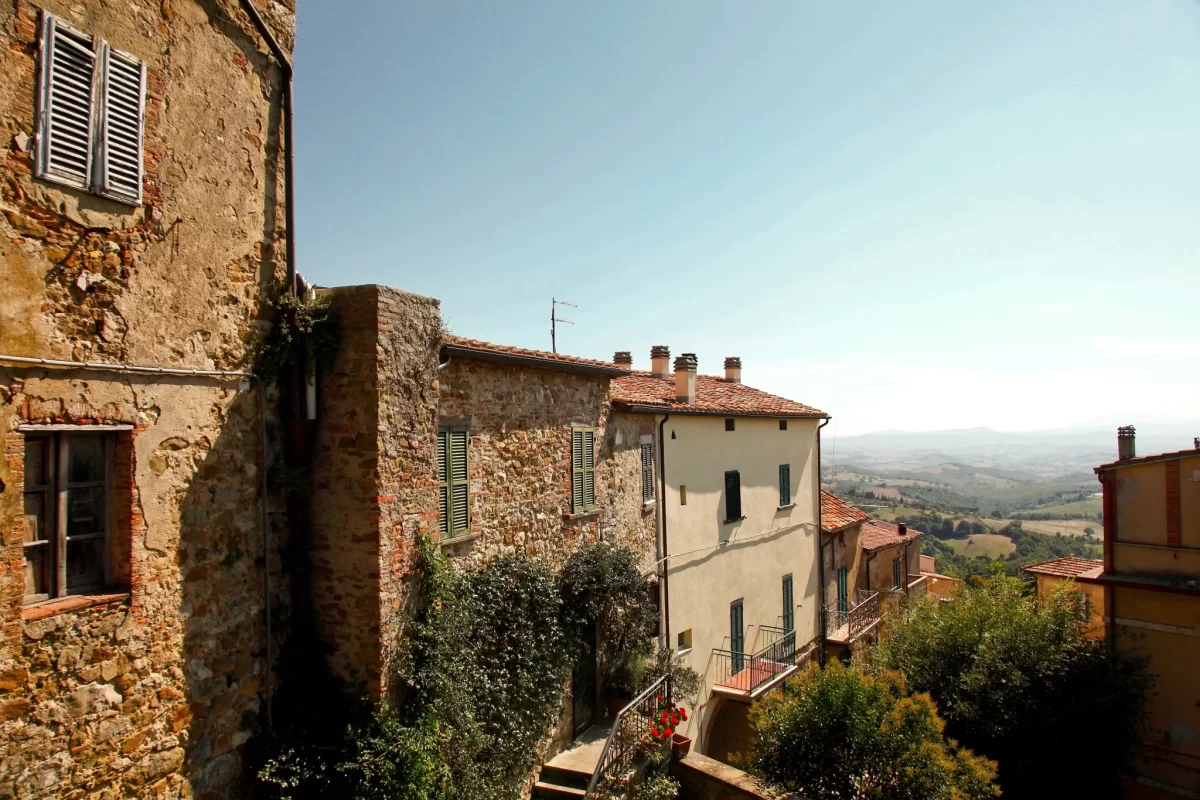 Vista su una città storica italiana con case in pietra e un paesaggio collinare sullo sfondo.