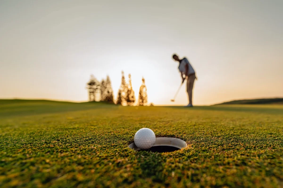 Giocatore di golf che mette mentre la pallina si avvicina alla buca al tramonto.
