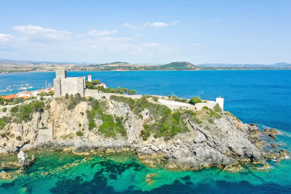 Vista aerea di un castello medievale su una scogliera affacciata su un mare azzurro.