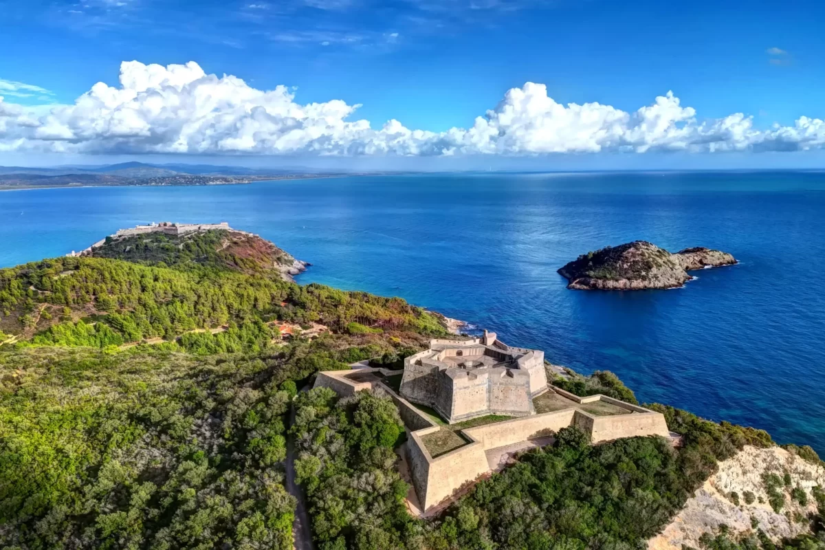 Fortezza in pietra circondata da un paesaggio costiero con isole e mare azzurro.