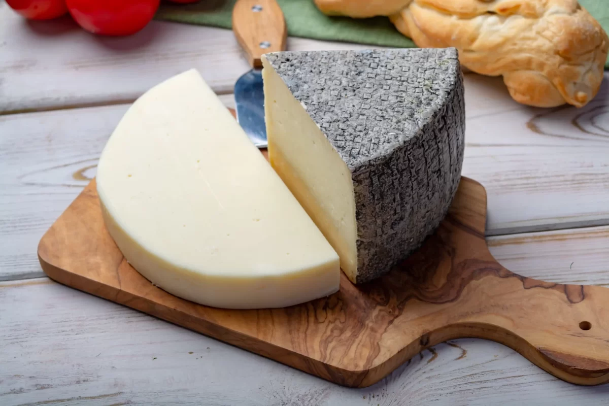 Formaggio semi-duramente affettato su un tagliere di legno.