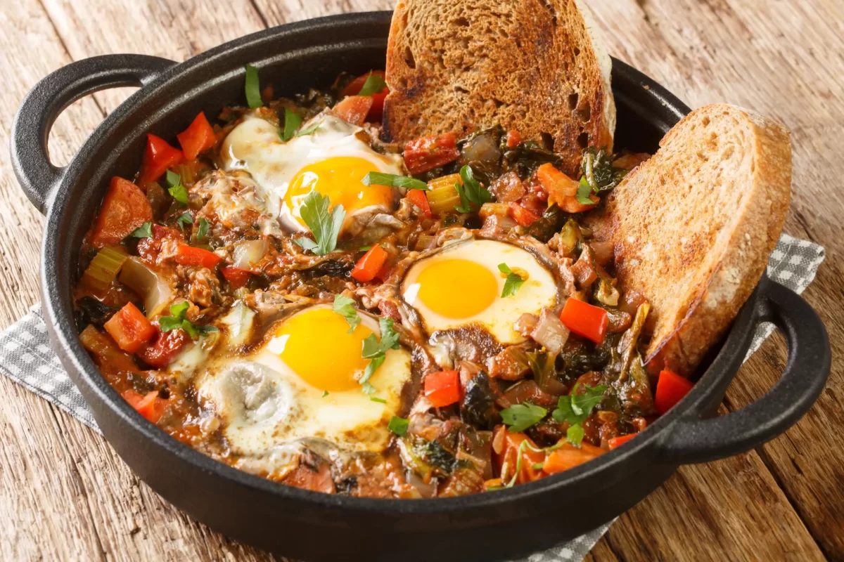 Padella di shakshuka con uova cotte, verdure e fette di pane.