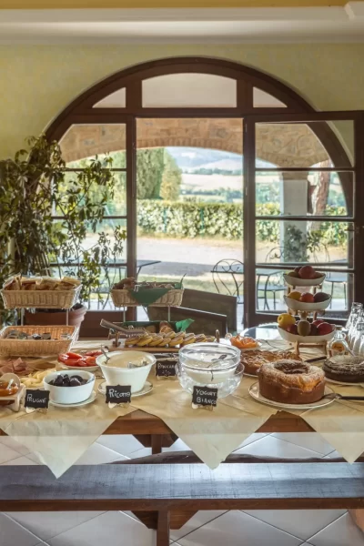Buffet per la colazione con dolci, bevande e frutta in una sala accogliente.