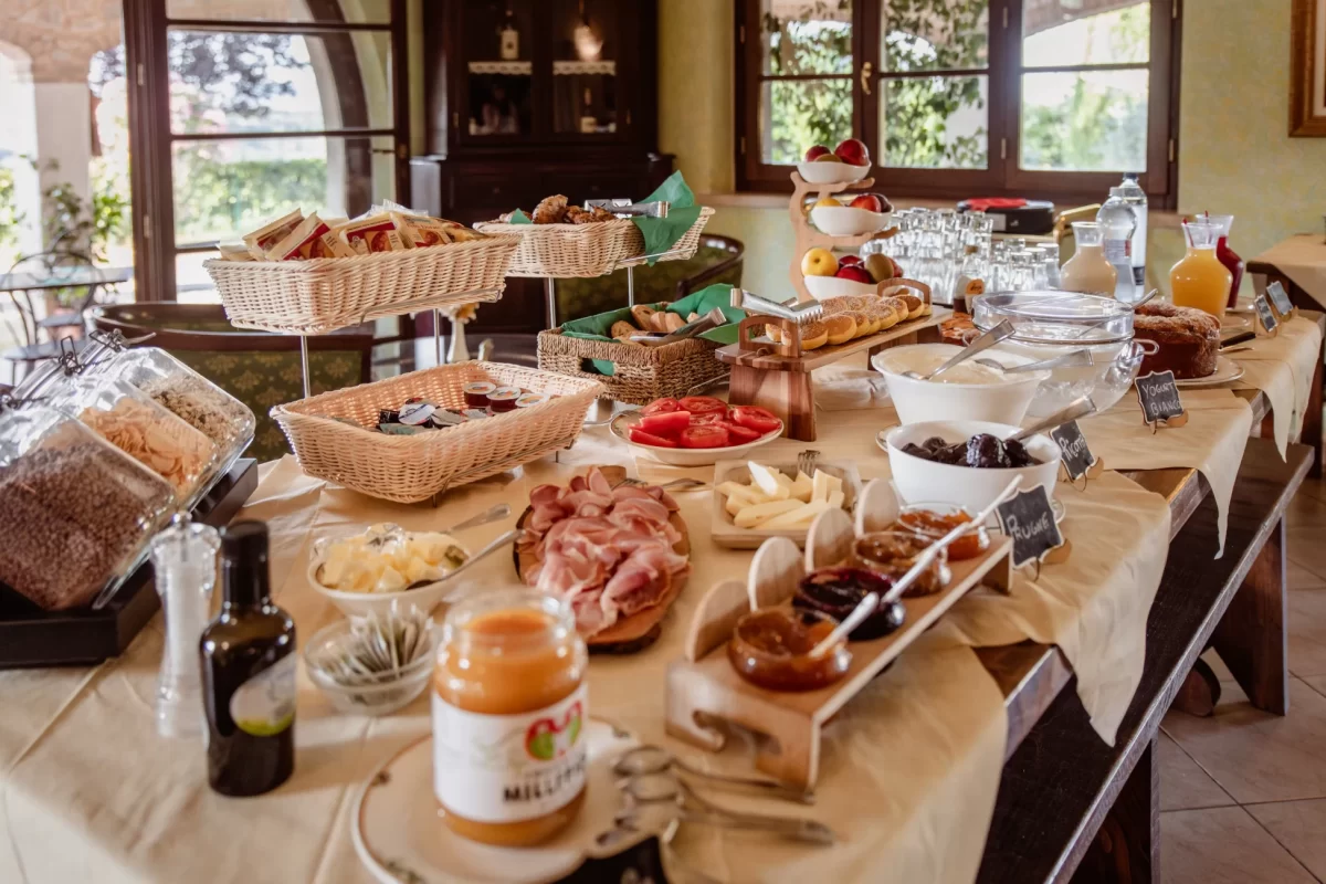 Buffet di colazione ricco di variet&agrave; con salumi, formaggi, frutta, cereali e succhi in un ambiente accogliente.