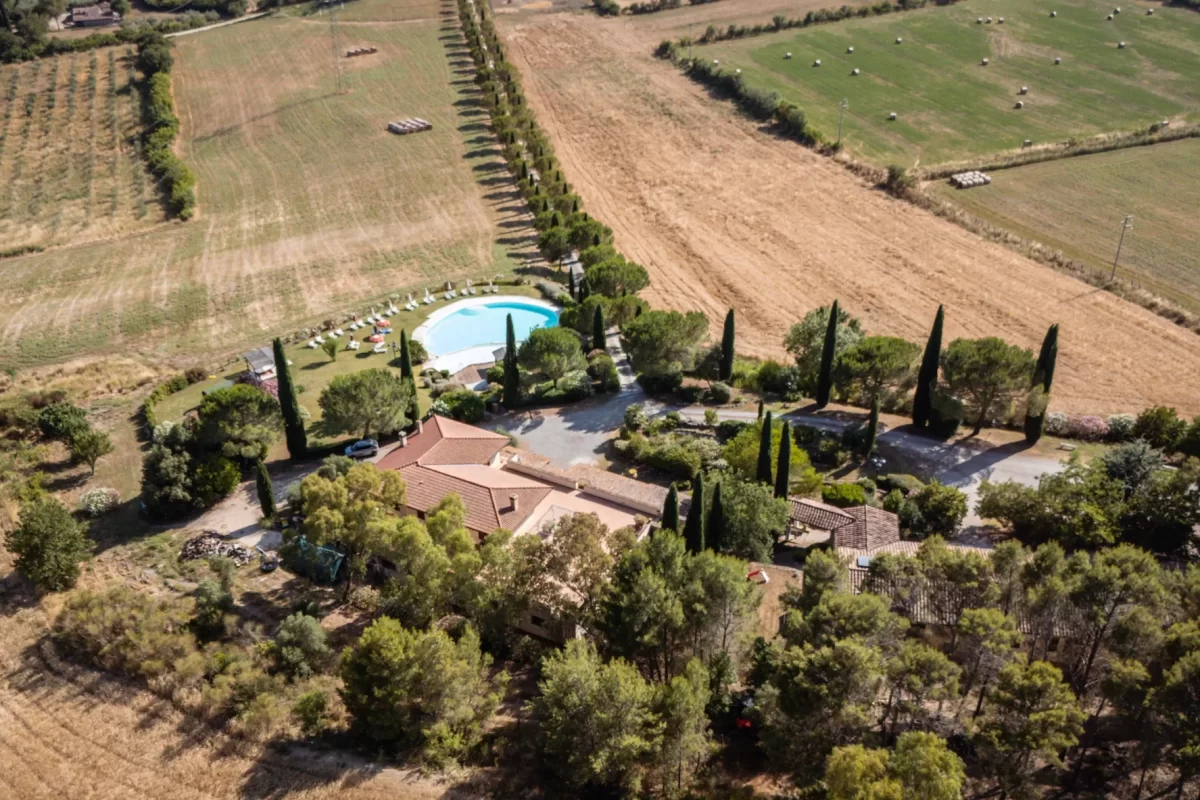 Vista aerea di una proprietà rurale con piscina circondata da campi e alberi.