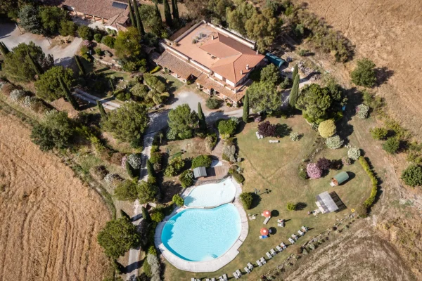 Veduta aerea di una villa con piscina circondata da un ampio giardino e campi.