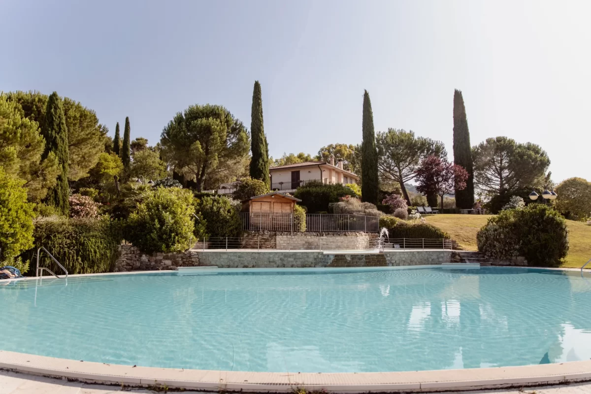 Piscina all'aperto con giardino e villa sullo sfondo.