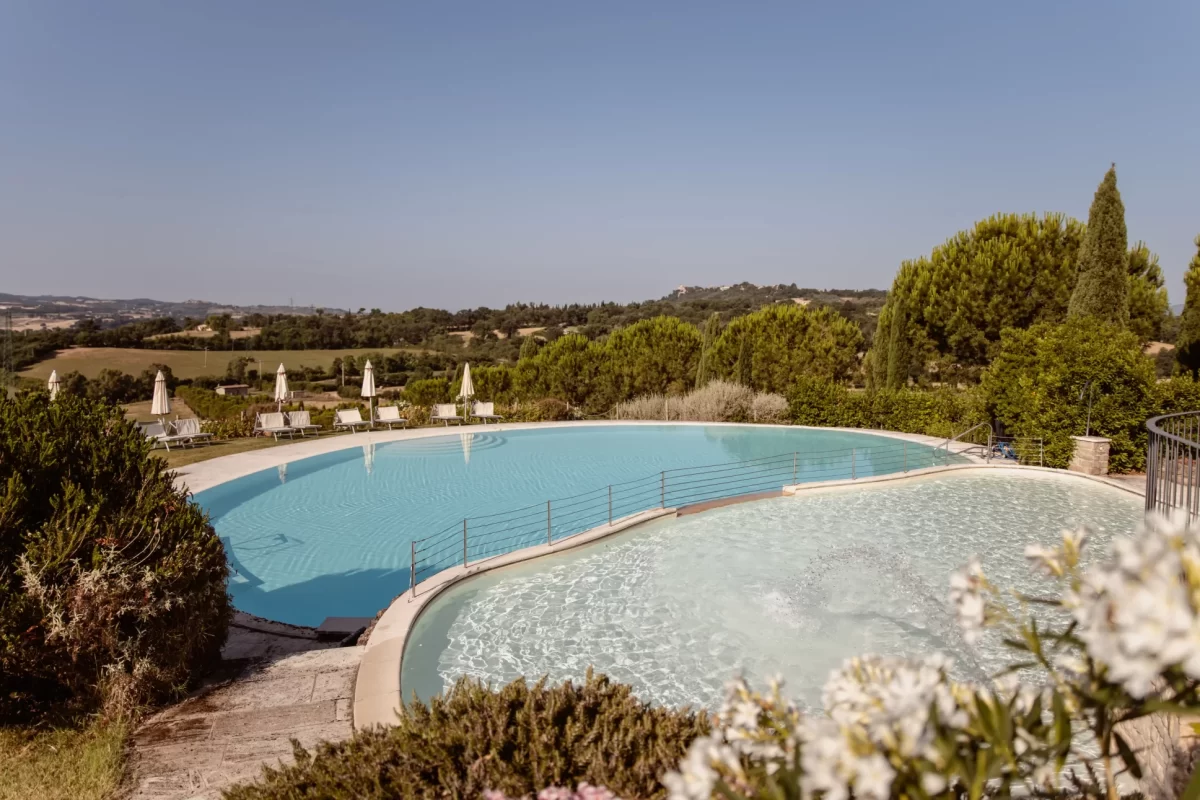 Piscina panoramica circondata da alberi con vista su colline verdi.