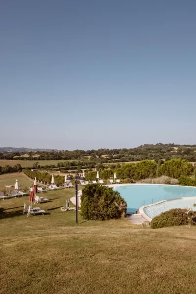 Piscina panoramica immersa nella campagna collinare con lettini e ombrelloni.
