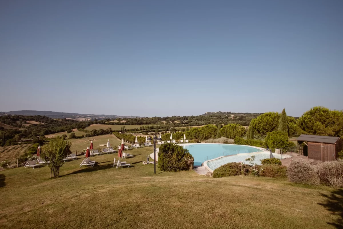 Piscina panoramica immersa nella campagna collinare con lettini e ombrelloni.