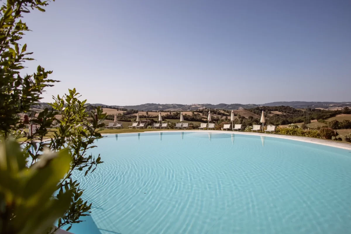 Piscina con vista su colline soleggiate e lettini con ombrelloni.