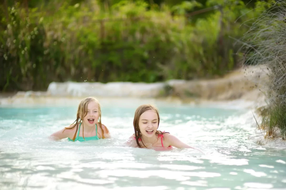 Due bambine che nuotano felicemente in una piscina naturale.
