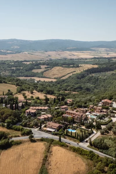 Vista aerea di un paesaggio collinare con campi, alberi e un piccolo borgo.