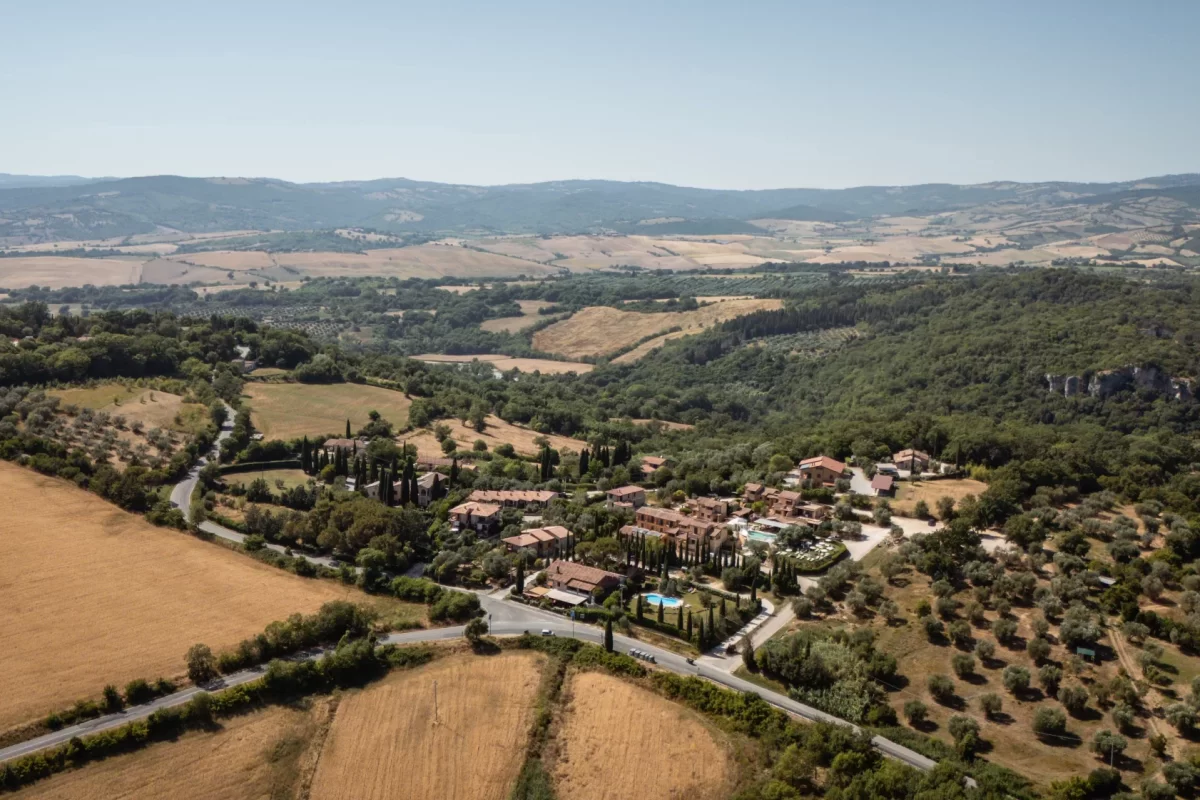 Vista aerea di un paesaggio collinare con campi, alberi e un piccolo borgo.