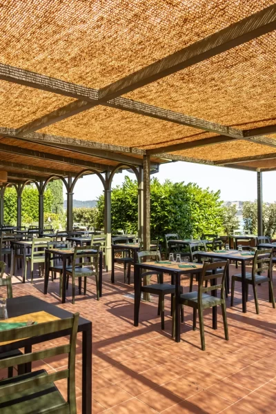 Terrazza di un ristorante all'aperto con tavoli e sedie sotto una copertura in paglia.