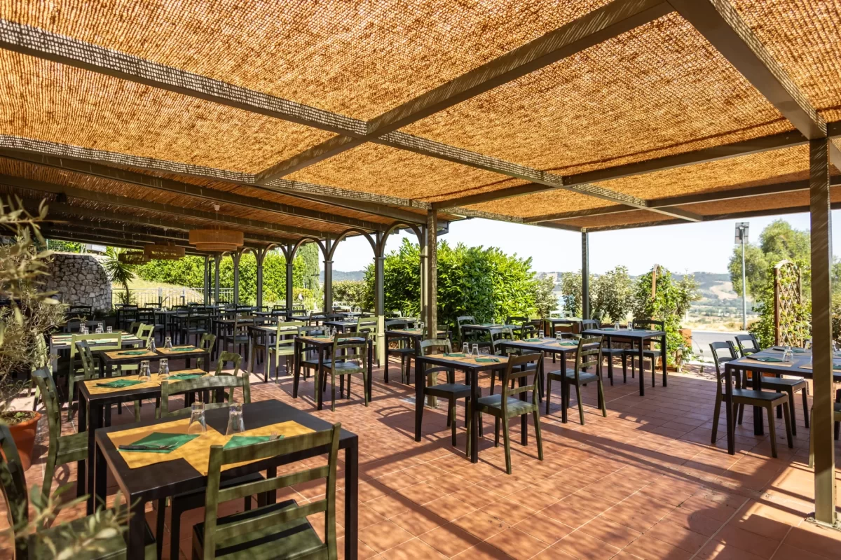 Terrazza di un ristorante all'aperto con tavoli e sedie sotto una copertura in paglia.