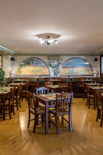 Interno di una sala ristorante con tavoli in legno e dipinti murali.